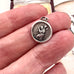 Silver vintage St Chrisopher charm held between fingers with a blurred background