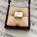 Silver vintage suitcase charm with 'SYDNEY' engraved on it in a jewelry box with music sheet background