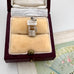 Vintage silver wishing well charm in an open jewelry box on a textured surface