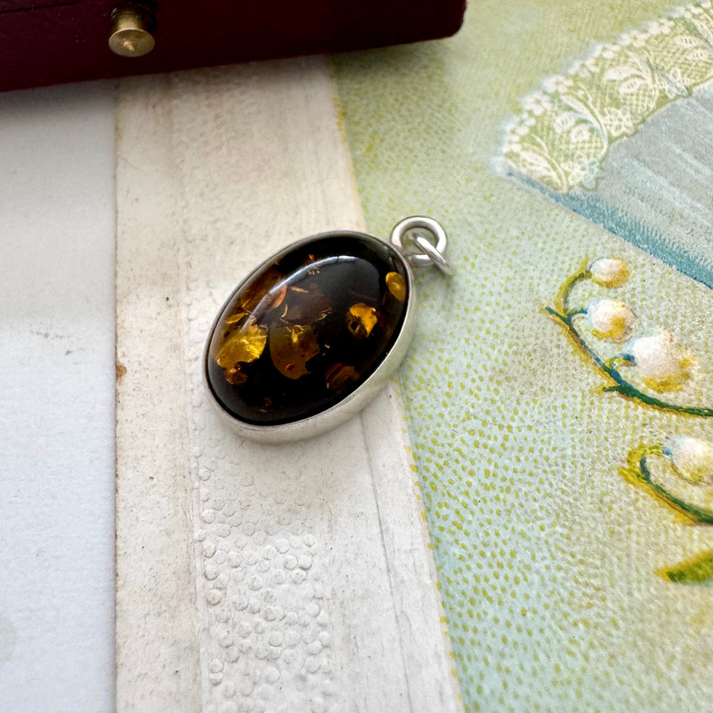 Silver pendant with embedded amber on a textured fabric background