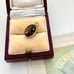 Amber pendant in a silver setting inside an open jewelry box on a textured surface.