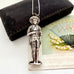 Vintage sterling silver needle case in the form of a boy holding a bunch of flowers. There is a vintage postcard and jewellery box in the background.