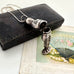 Vintage sterling silver needle case in the form of a boy holding a bunch of flowers. There is a vintage postcard and jewellery box in the background.