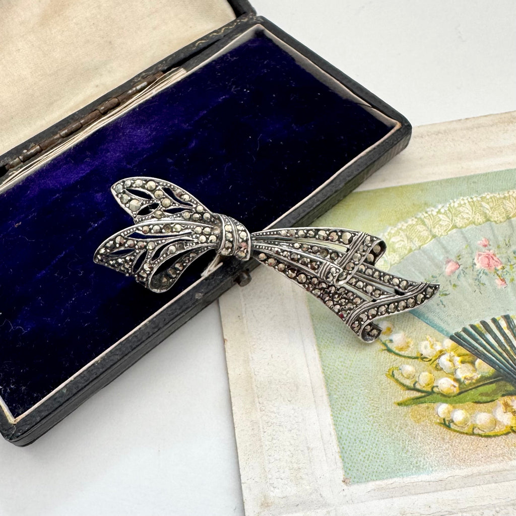 Silver and marcasite bow-shaped brooch in a black velvet box on a decorative card.