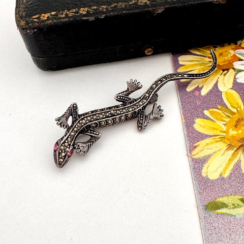 Vintage sterling silver lizard brooch on a white surface with a floral card in the background