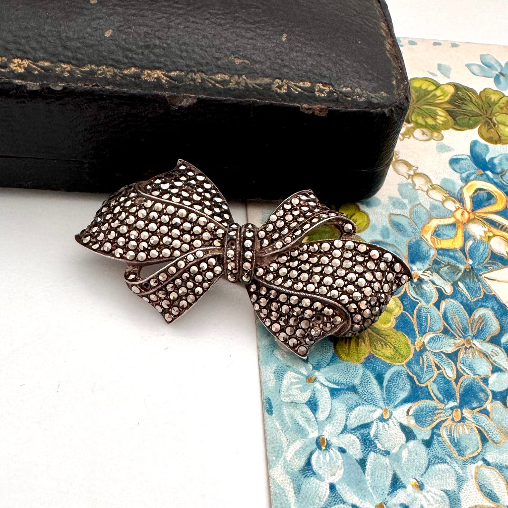 Silver bow-shaped brooch on a floral-patterned surface