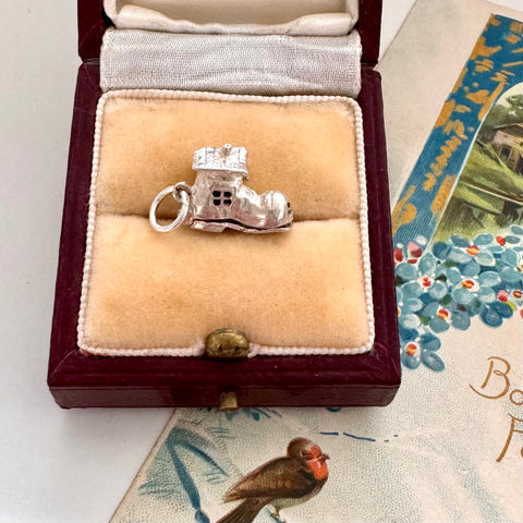 Vintage silver old woman in a shoe charm in a jewelry box on a decorative surface with floral patterns. 