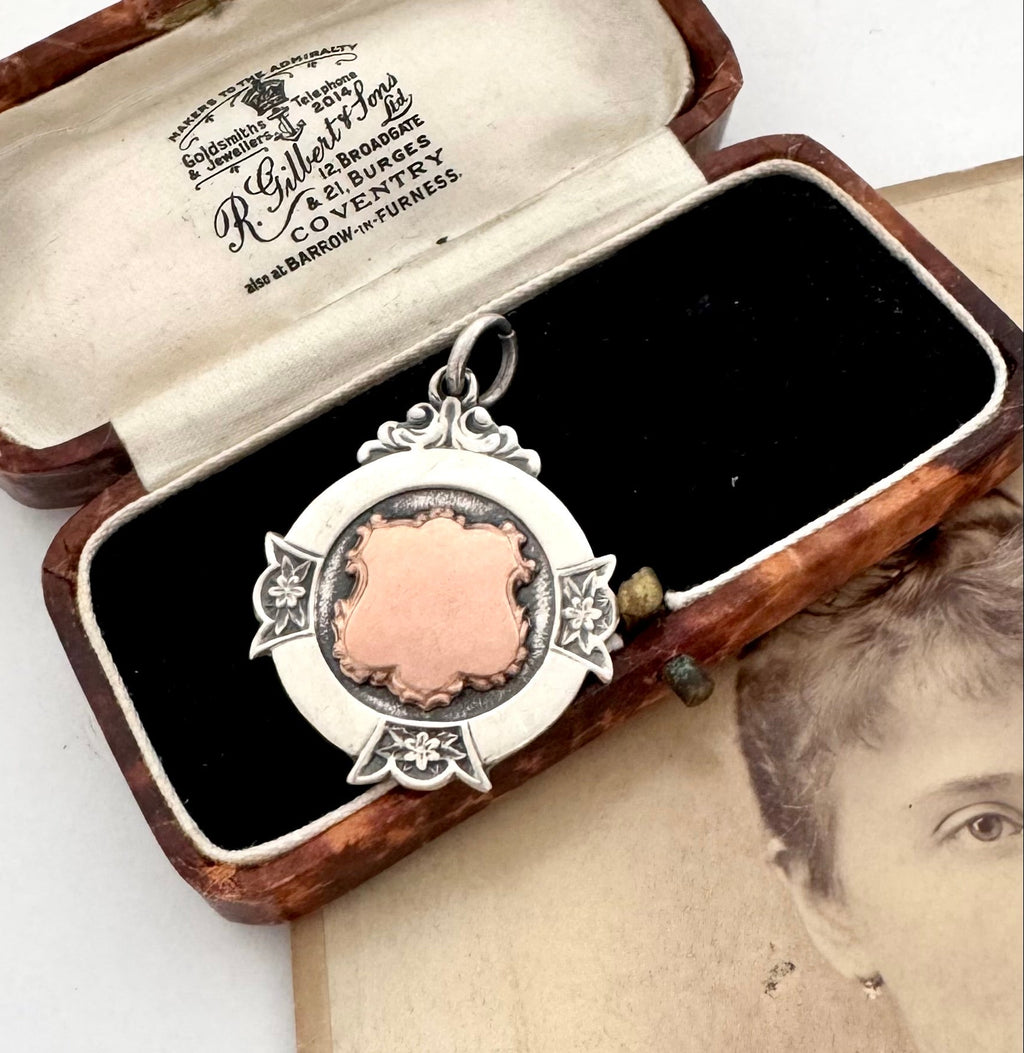 A sterling silver vintage watch fob pendant with a rose-gold heart-shaped center, displayed inside an open vintage wooden presentation box with black velvet lining.