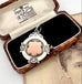 A sterling silver vintage watch fob pendant with a rose-gold heart-shaped center, displayed inside an open vintage wooden presentation box with black velvet lining.
