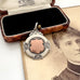 A vintage sterling silver watch fob pendant with a rose-gold shield-shaped center, displayed next to its original wooden and velvet box on top of an antique sepia portrait photograph.