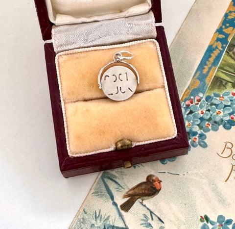 Vintage silver spinning "Good Luck" charm in a wooden box on a floral-patterned surface