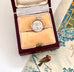 Vintage silver spinning "Good Luck" charm in a wooden box on a floral-patterned surface