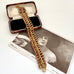 A vintage gold-toned chain bracelet with a curb link pattern, displayed diagonally across an open vintage presentation box and a black-and-white portrait print on a white surface.