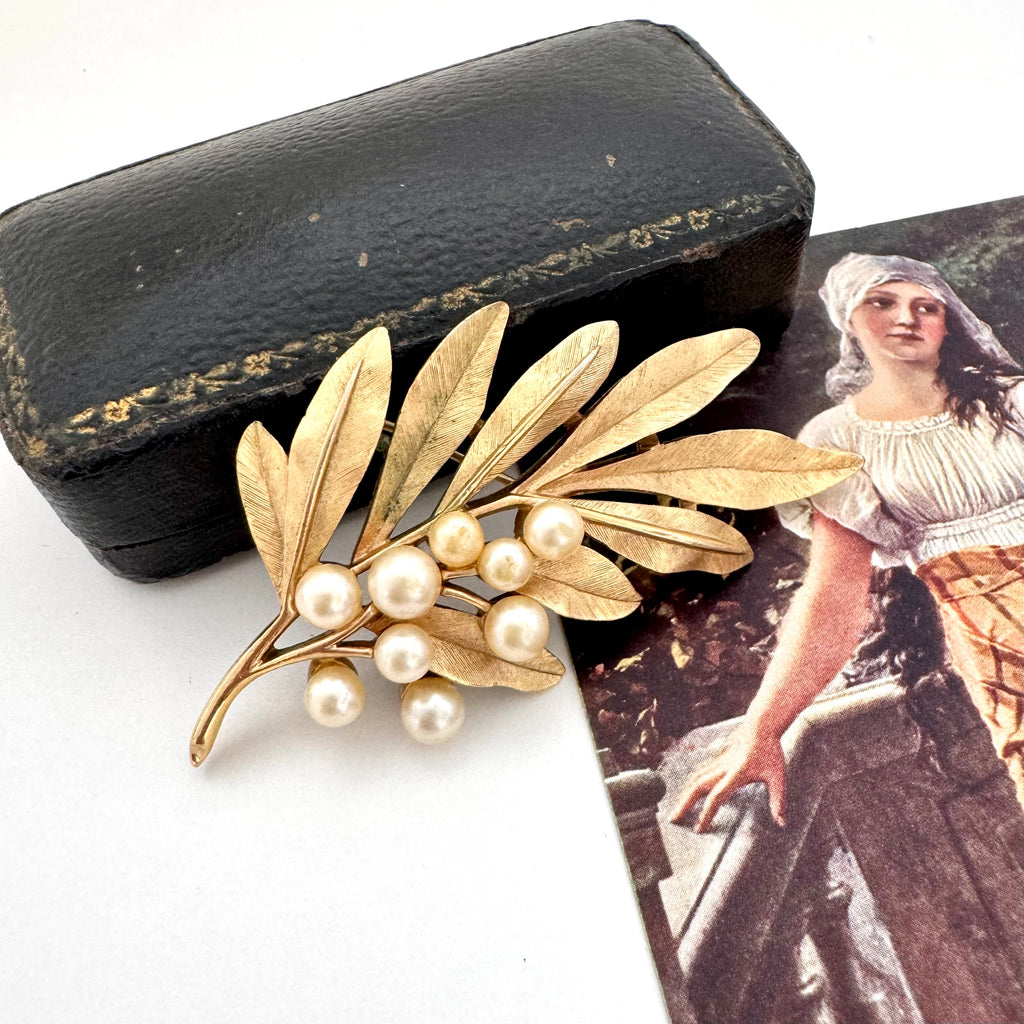 Trifari vintage gold leaf and pearl brooch with a black case and vintage illustration in the background