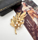 Trifari vintage gold leaf and pearl brooch with a black case and vintage illustration in the background