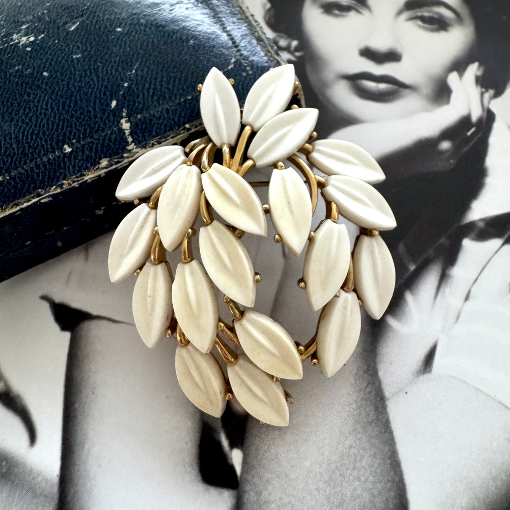White vintage Trifari leaf-shaped brooch on a black background with a vintage photo of a woman.