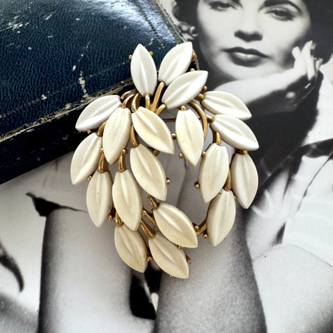 White vintage Trifari leaf-shaped brooch on a black background with a vintage photo of a woman.