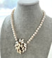 Pearl necklace with a leaf-shaped pendant on a gray mannequin bust.
