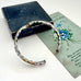 Vintage white cloisonne hinged bangle on an old jewellery box and with an old floral postcard