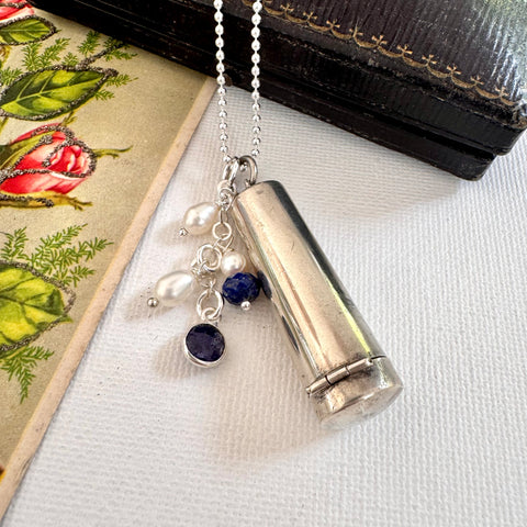 Vonk Jewellery 1922 silver cheroot case necklace with lapis and pearl charms on a white background with a vintage postcard and box