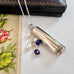 Vonk Jewellery 1922 silver cheroot case necklace with lapis and pearl charms on a white background with a vintage postcard and box