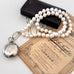 Pearl necklace with a silver pocket watch on an old document