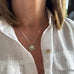 Image of a woman's neck. She is wearing a vonk Jewellery 1911 sixpence necklace and a white linen shirt