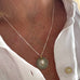 Image of a woman's neck. She is wearing a vonk Jewellery 1911 sixpence necklace and a white linen shirt