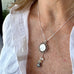 Image of a woman's neck. She is wearing a Vonk jewellery coin and pearl necklace and a white linen shirt