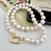 A strand of lustrous white freshwater pearls arranged in a loop with a gold clasp, photographed on a light fabric surface with vintage paper and a black case as styled props.
