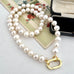 A strand of white freshwater pearls with a gold clasp, arranged on a vintage floral card next to an open black jewelry box.