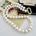 A strand of white freshwater pearls with a gold clasp, draped over a vintage floral card and resting on a black jewelry box.