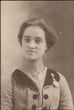 A vintage sepia-toned portrait photograph of a young woman wearing a textured tweed jacket with a dark collar and a decorative brooch.