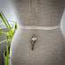 Antique 9ct gold watch key with charms on a small mannequin and with leaves in the background.