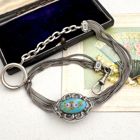 Antique French silver albertina chain with an oval turquoise and floral enamel centerpiece, displayed next to an open dark box on a light fabric surface.