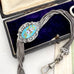 Antique French silver albertina chain with an oval enamel centerpiece, displayed inside an open dark presentation box with a purple velvet lining.