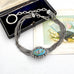 Antique French silver albertina chain with an oval turquoise and floral enamel centerpiece, displayed on a white surface with an open black presentation box and a decorative card in the background.