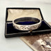 Antique Silver bracelet with floral patterns in an open box on a white background