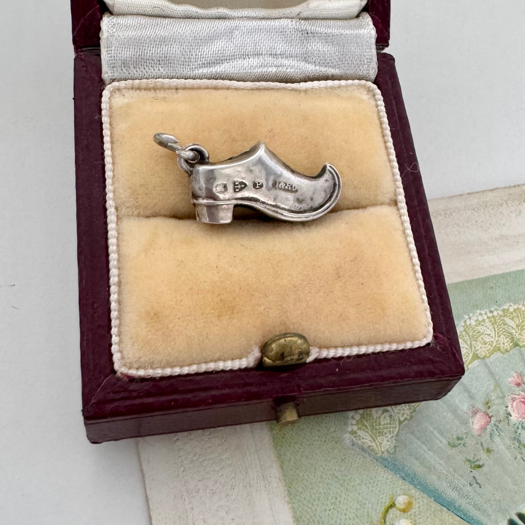 Antique silver shoe charm in a jewelry box on a textured surface
