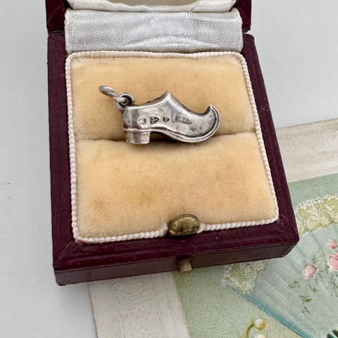 Antique silver shoe charm in a jewelry box on a textured surface