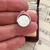 Silver vintage spinning I Love You charm held between fingers on a sheet of music
