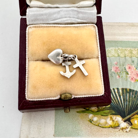 Silver faith, hope and charity charm in a jewelry box with a fan and pearls in the background