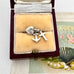 Silver faith, hope and charity charm in a jewelry box with a fan and pearls in the background