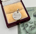 Silver pendant with engraved name in a velvet box, with a vintage photo in the background.