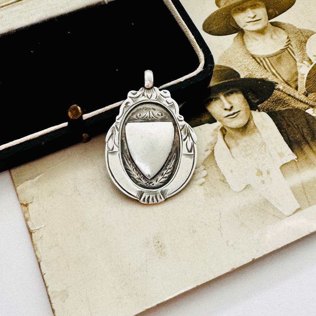 Vintage 1932 Fattorini sterling silver 1932 watch fob pendant with ornate detailing, displayed on top of an antique sepia-toned photograph and a black jewelry box.
