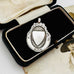 Vintage 1932 Fattorini sterling silver 1932 watch fob pendant with ornate detailing, displayed on top of an antique sepia-toned photograph and a black jewelry box.
