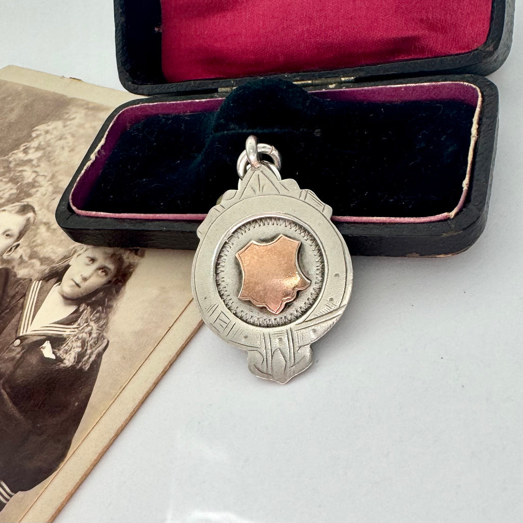 Vintage silver and rose gold pendant in an open velvet box with an old photograph underneath.
