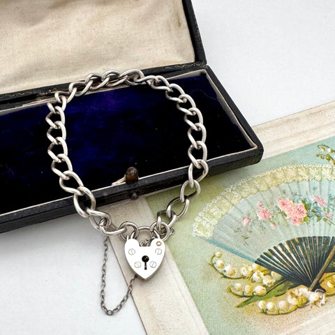 Silver chain bracelet with a heart-shaped lock charm on a vintage-style card.