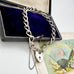 Silver chain bracelet with a heart-shaped lock on an antique box and fan in the background