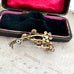 Back of a vintage floral brooch on a textured surface with an open jewelry box in the background